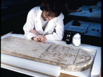Conservator Suzanne Davis works in the lab on a large stone stela, cleaning its surface with a cotton swab.