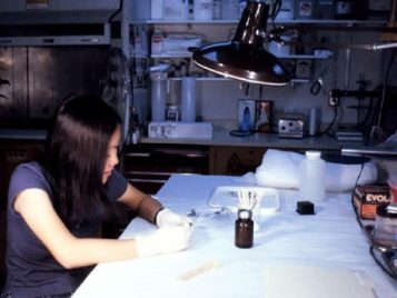 An undergraduate student works in a lab setting, using cotton swabs to work on bronze objects.