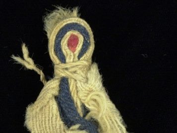 Ancient doll made out of red, blue, and white cloth bundled together.