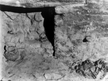 Archival photo of a group of textiles in situ in the corner of a mudbrick house at Karanis, Egypt.