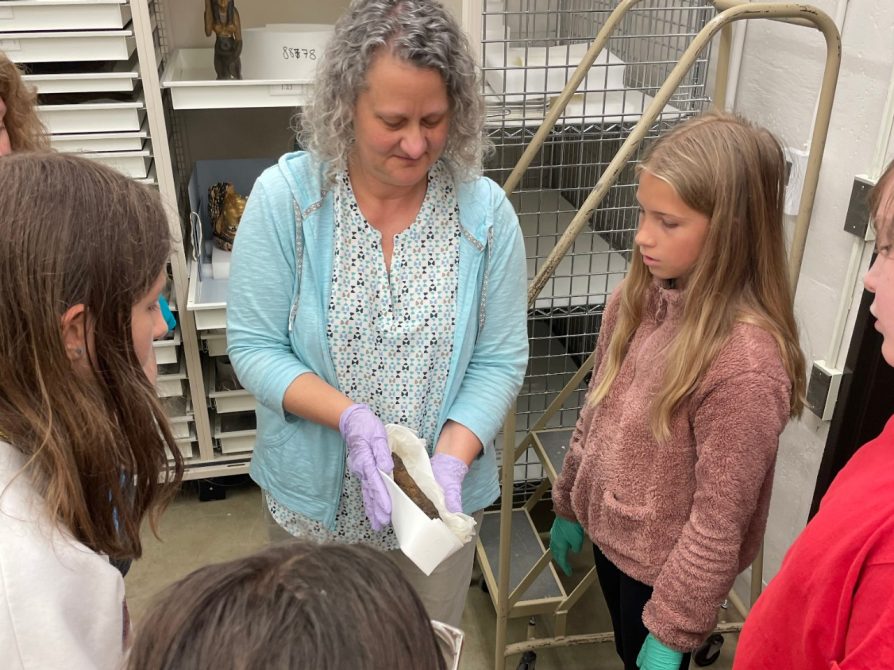 Kelsey Registrar Michelle Fontenot, with gloved hands, shows a group of middle-schoolers a hawk mummy.