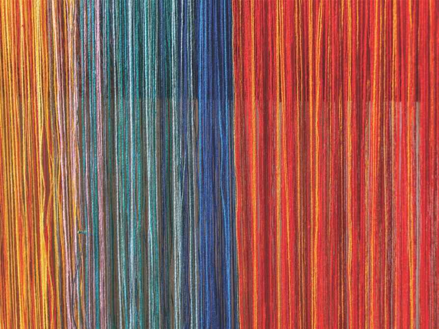 Close-up of bright yellow, green, blue, and red threads pulled taut.