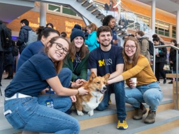 Students crouching around Reggie the Campus Corgi