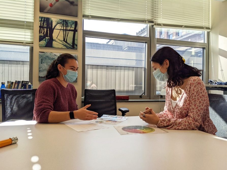 Sarah Renberg, a graduate of the Honors Program at the University of Michigan College of Literature, Science, and the Arts, is pictured at a table with another student. They both wear medical masks.