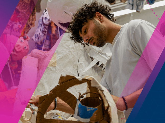 A student is pictured working on a large paper mache sculpture surrounded by numerous other already finished sculptures. 