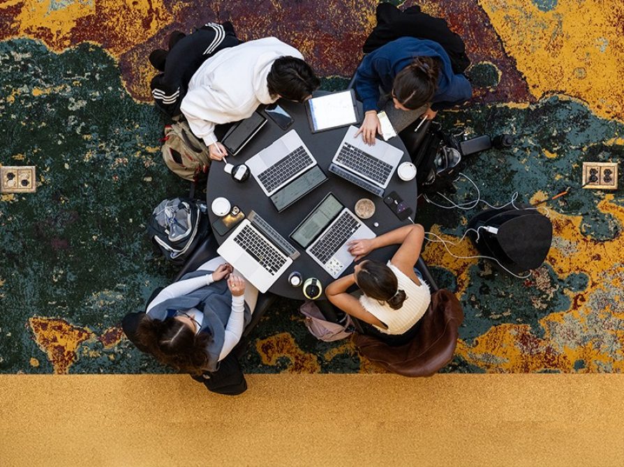 bird's eye view of four students working on their laptops around a round table