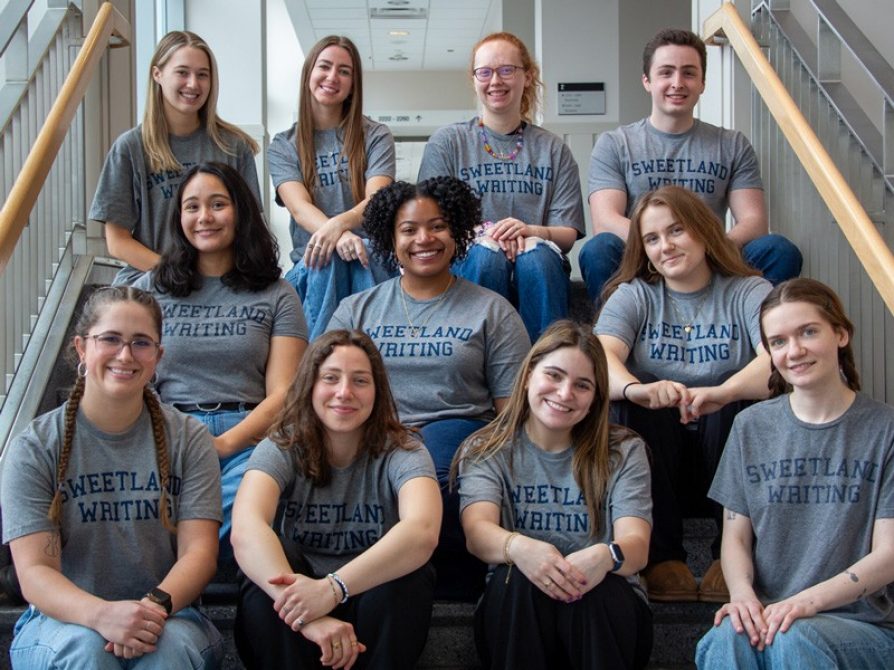 group photo of class members sitting on steps in a hallway on campus
