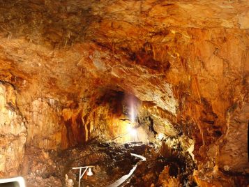A large, deep cave lit towards the back that has a wooden walkway down the center surrounded by stalagmites .