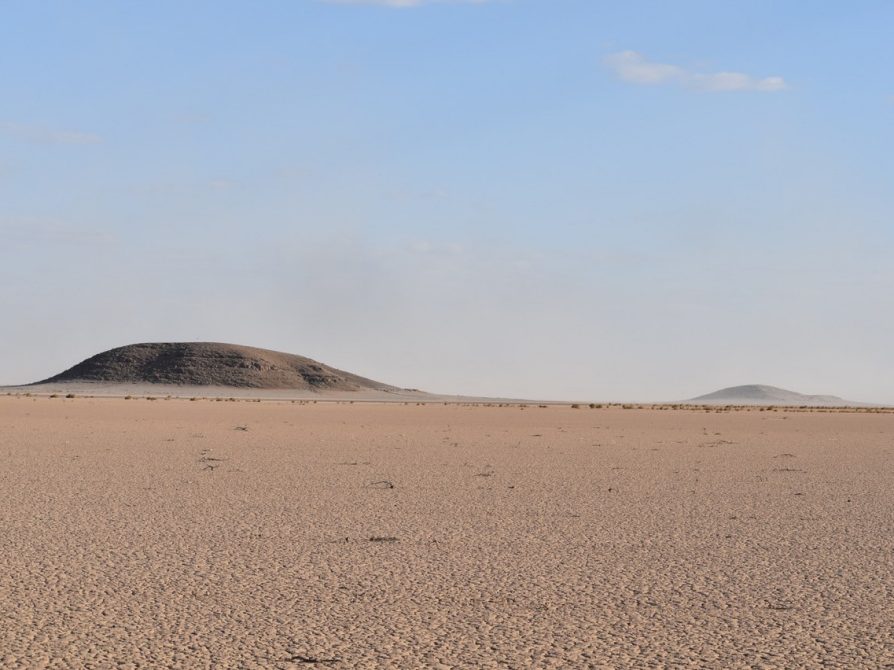 Photo of wide flat desert and blue sky with two hills in the distance
