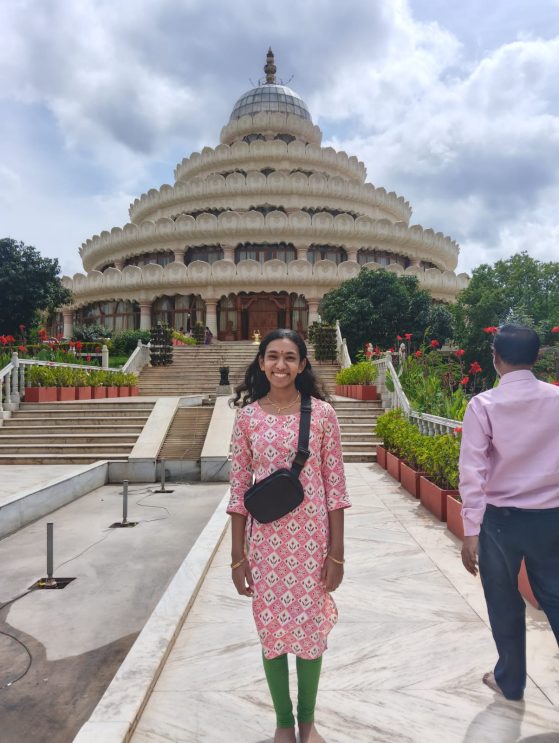 Vishalakshi Meyyappan stands in front of an ornate building while smiling