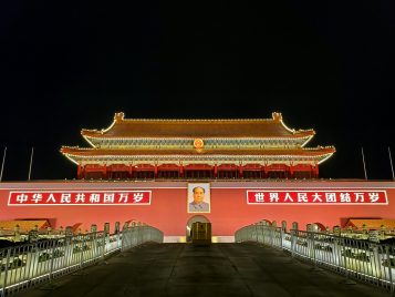 Red and gold lit up asian style building at the end of a bridge