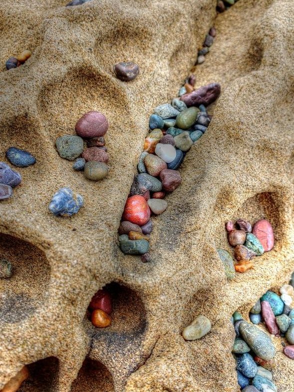 Sand with natural divets that are filled with colorful stones.