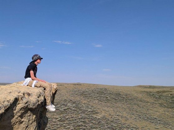 Caton sitting on a rock outcrop looking out across wide open land to the horizon.