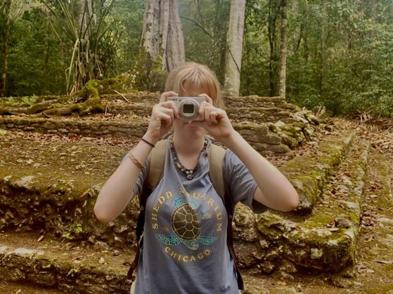 Humphrey standing in front of a short stack of stone steps, taking a picture of the person taking a picture of her.