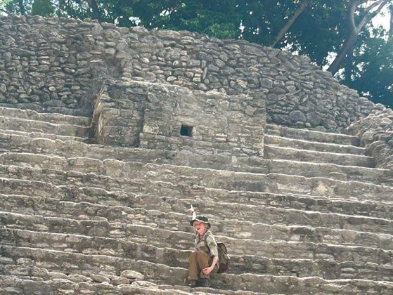Humphrey sitting on the steps about 1/3 of the way up a Mayan temple pointing to a square opening about 2/3 of the way to the top of the temple.