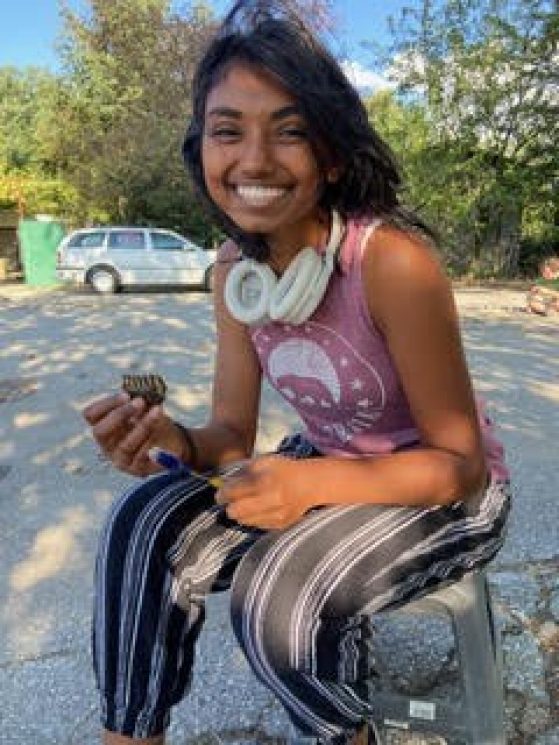 Nama seated on a stool artifact in one hand, cleaning tool in the other.