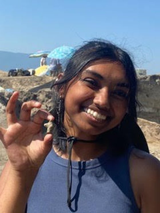 A close-up of a smiling Nama holding a small, three-pronged artifact.