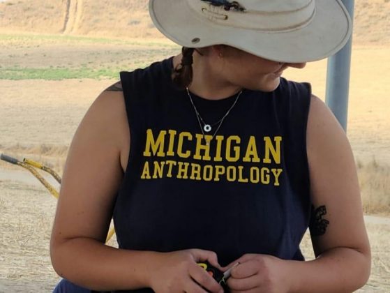 Tutak, holding a tape measure, looking off camera at what's going on at the excavation site.