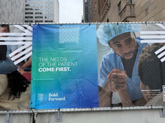 Banner on a street barrier reads, "The needs of the patient come first." Mayo Clinic logo with "Bold. Forward." tagline.