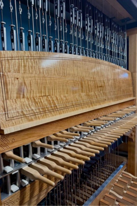 Close-up of a wooden carillon keyboard with wooden batons and pedals, showing intricate levers and polished wood grain.