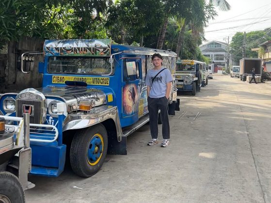 A brilliant blue bus with Atkinson standing in front of the mural on its side.