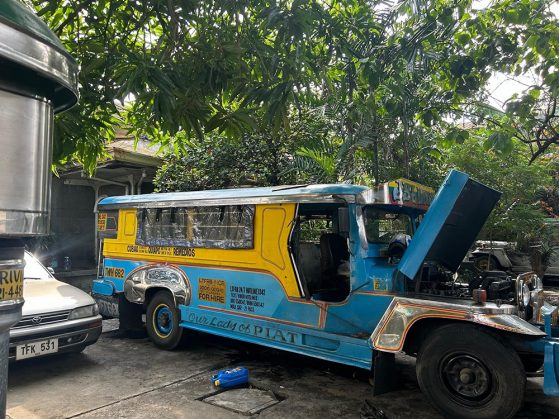 Side view of a blue and yellow bus with its door open and hood up that says Our Lady of PIAT down the running board.
