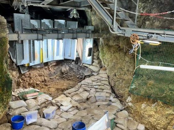 Small cave space with stone floor, walls of stone and metal, with the ceiling of metal stairs.