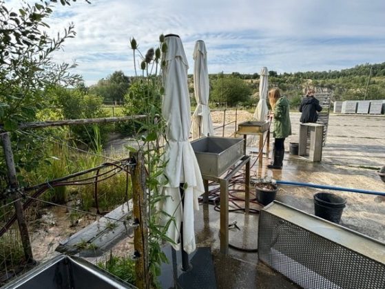 Two researchers standing at tables topped with rectangular metal boxes using water to screen sediment extracted from Hohle Fels.