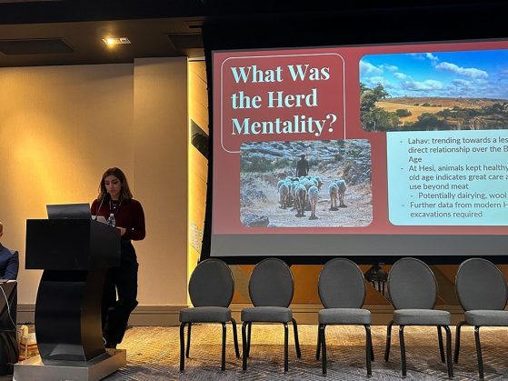 Pruette standing at a podium talking about the project titled, "What Was the Herd Mentality?" that contains photos of the area and of a shepherd leading his herd.