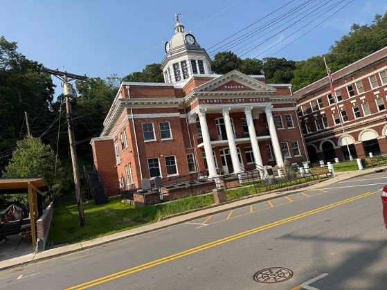 Red brick Madison County Courthouse with white columns, clock tower, and American flag, viewed from across the street.