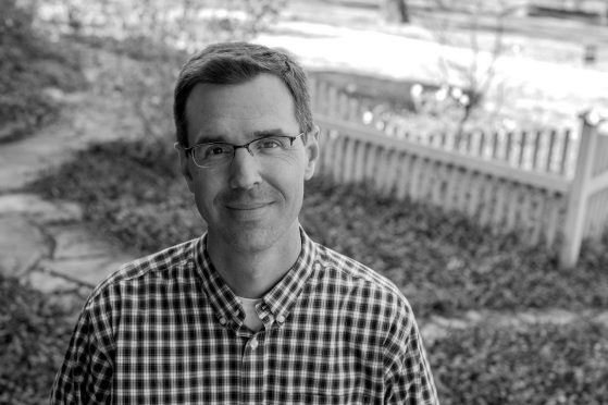 Black and white photo of Eric McHenry in front of a picket fence