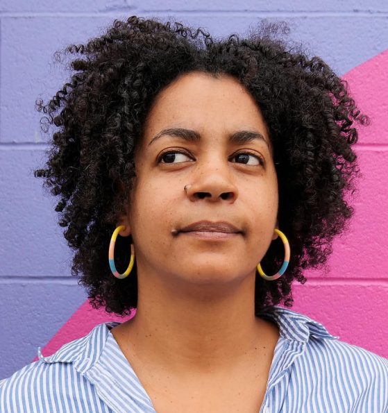 Headshot of Aisha Sabatini Sloan in a blue shirt in front of a pink and purple wall