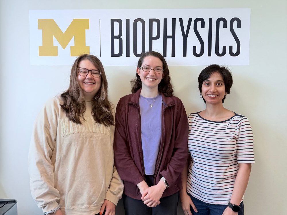 3 students posing in front of a biophysics sign.