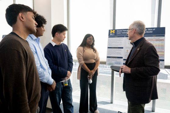 Students talking with person about their poster presentation.