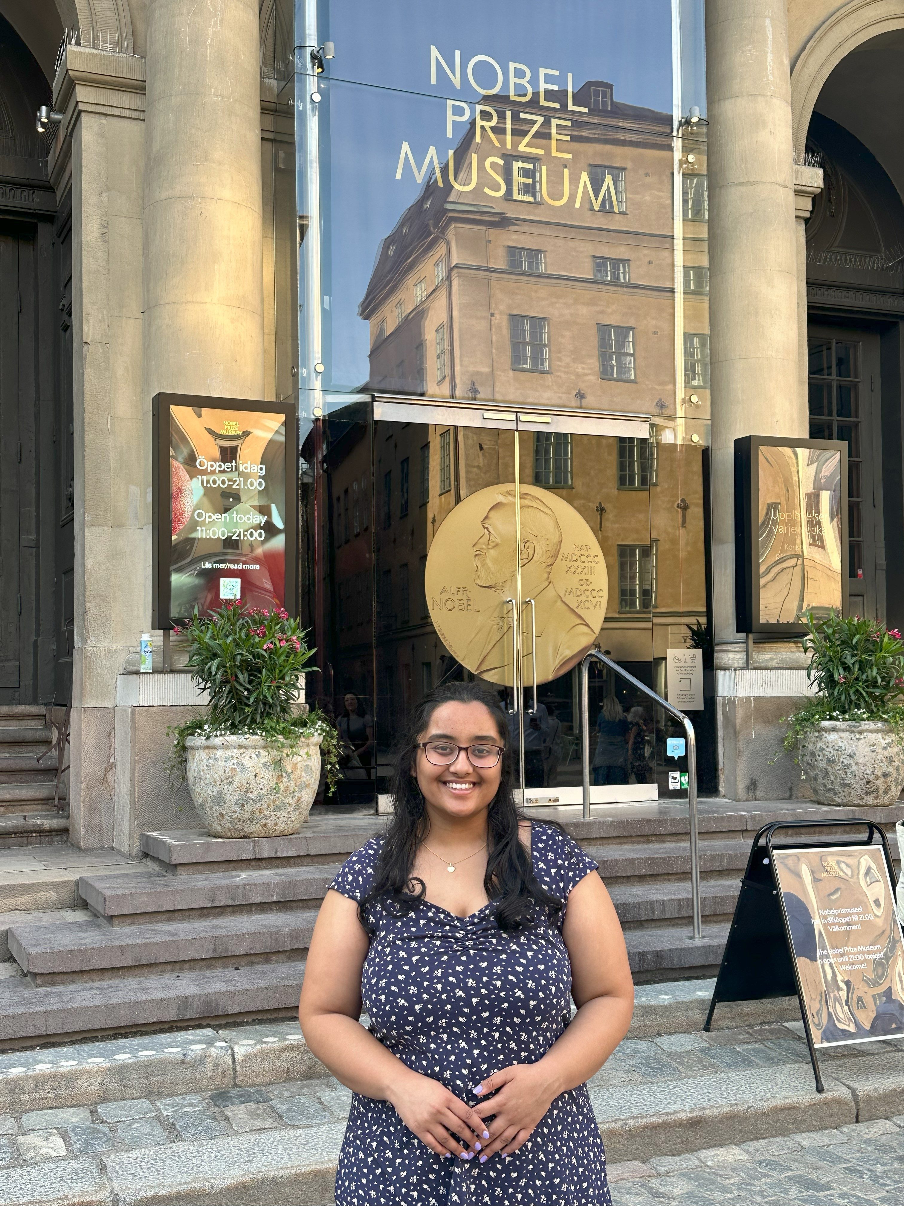 Nobel Prize Museum, Stockholm, Sweden. Pictured: Prema. Caption: Prema standing in from the the doors for the Nobel Prize Museum, an area highlighting the history, the founder, and the various discoveries of Nobel Prize Winners