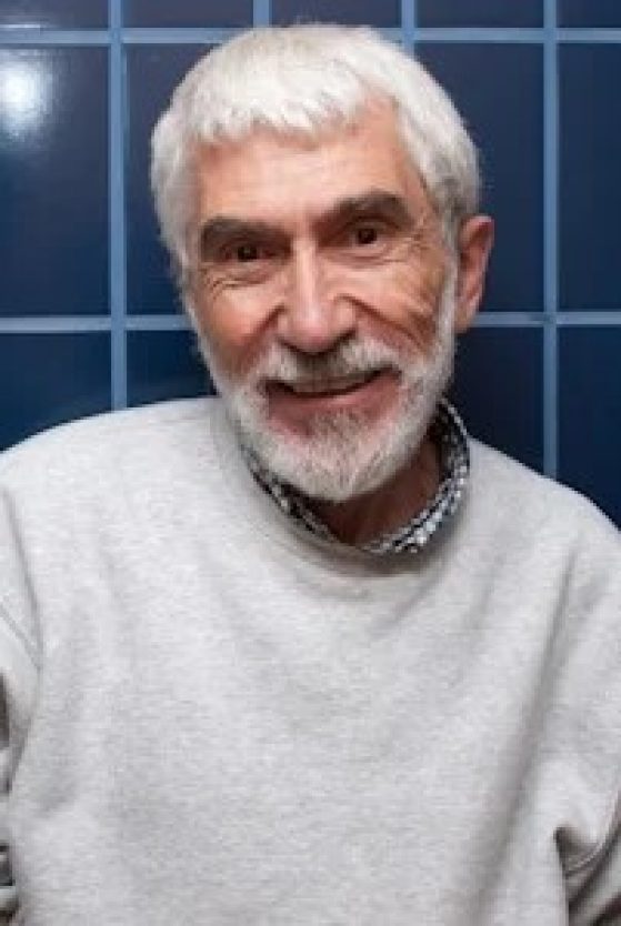 portrait of man with white hair in front of a blue tile wall