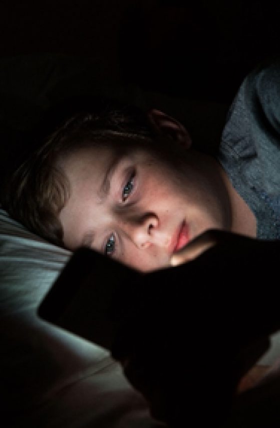 Child in bed, looking at phone.