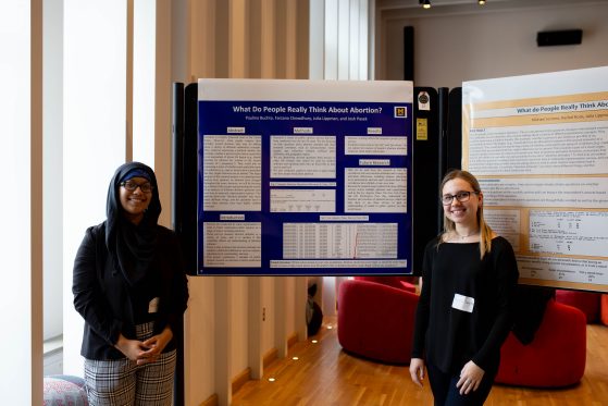 Two girls (presenters) standing in front of a poster marked with "distinction," smiling. Links to Undergraduate research day page