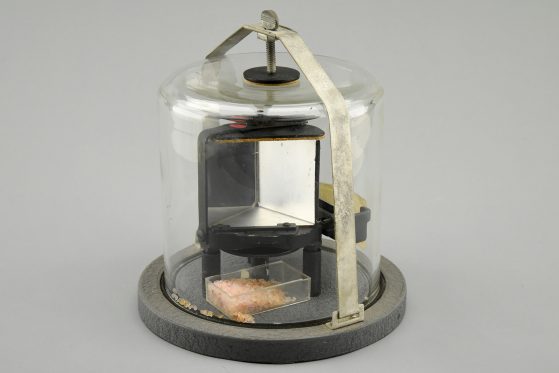 Photograph of metal-mounted salt prism inside glass bell jar with metal base and clamp holding it shut. Photograph by Dale Austin