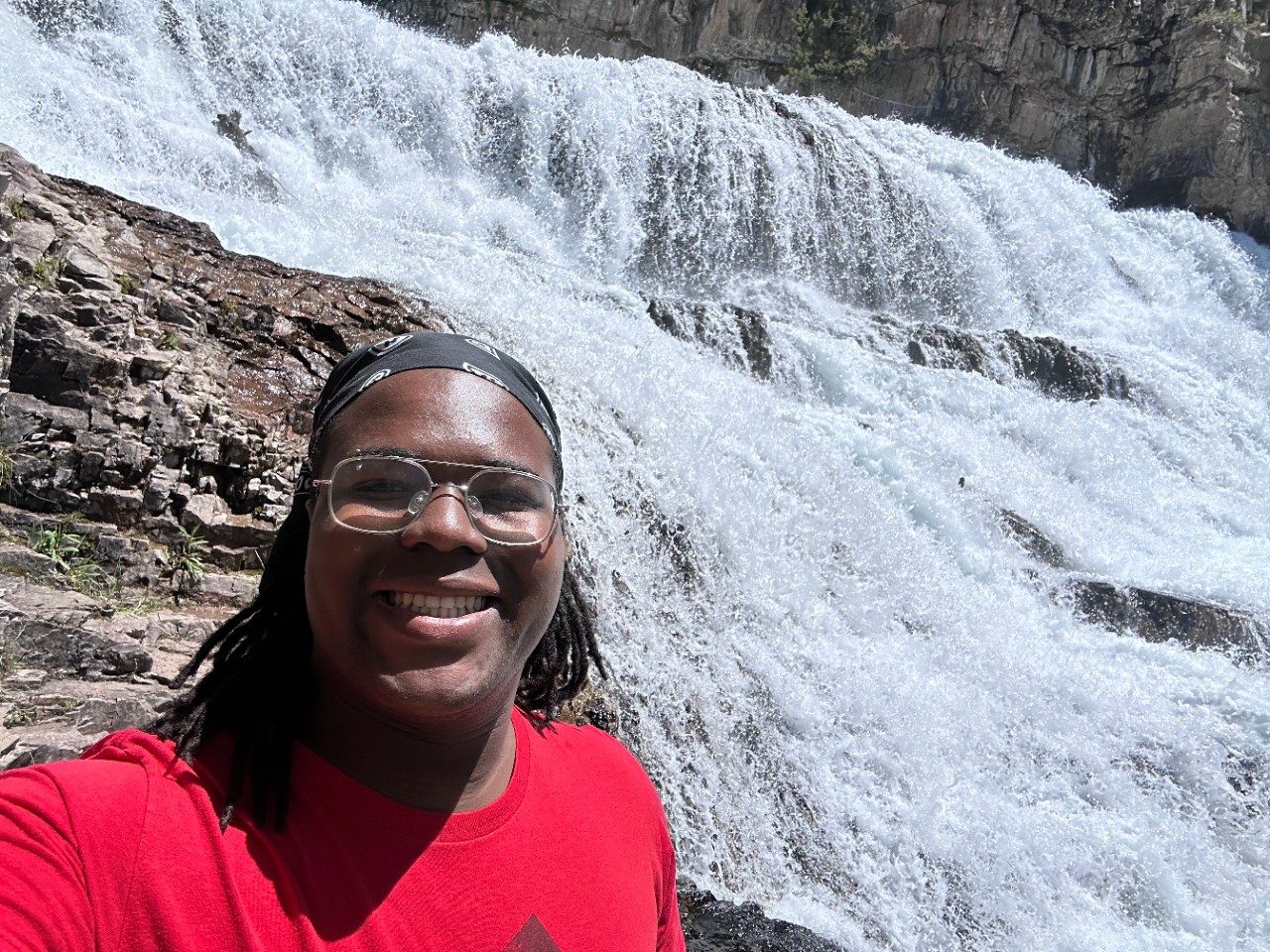 A man in glasses smiling in front of a waterfall