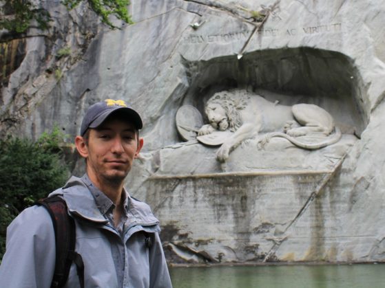 Micheal is pictured in front of a stonge carving of a sad, battle-worn lion. 