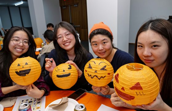 Four students show off orange paper jack-o-lanterns they decorated at the event