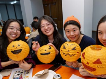 Four students show off orange paper jack-o-lanterns they decorated at the event