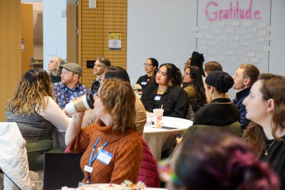 Attendees at the 2024 Closing Ceremony seated at round tables looking at listening towards a presenter