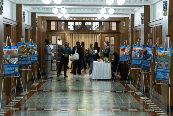 Event venue hallway showcasing sustainability information on posters and attendees entering the ballroom