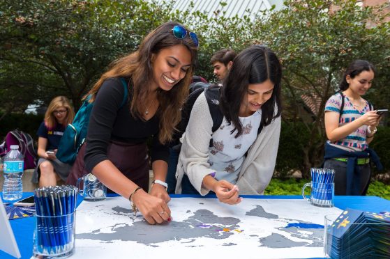 Two students participate in an outdoor activity with a map and stickers to be placed on the map.  Two other people are in the background.