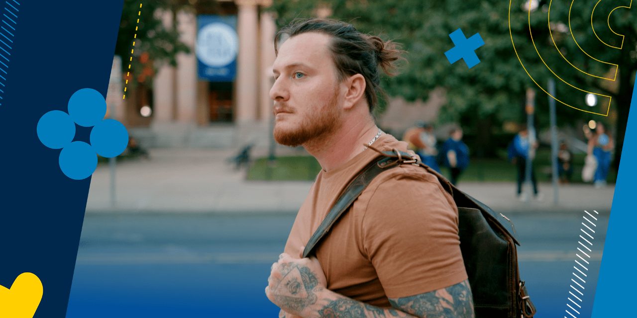 A student with a backpack strapped over his shoulder walks across campus.