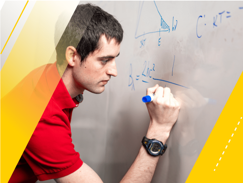 Ph.D, student, Rory Bowens, pictured in a red shirt, draws a formula on a whiteboard with a blue marker.