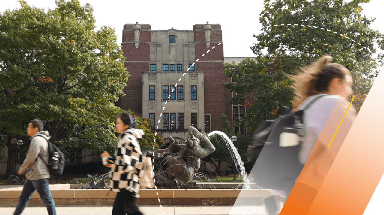 Three students walk in different directions past the fountain in front of the Michigan League. The fountain is spouting water. The leaves on the trees are green.