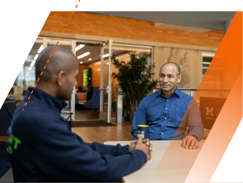 An LSA student and his alumni mentor sit in conversation at a table on the second floor of the LSA Building, upstairs from the LSA Opportunity Hub. 